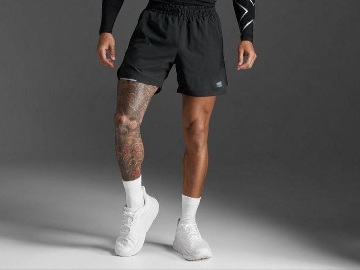 Man wearing black athletic outfit with white sneakers on a gray background